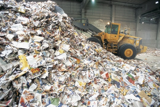 Un tractopelle charrie des montagnes de papier dans un centre de recyclage