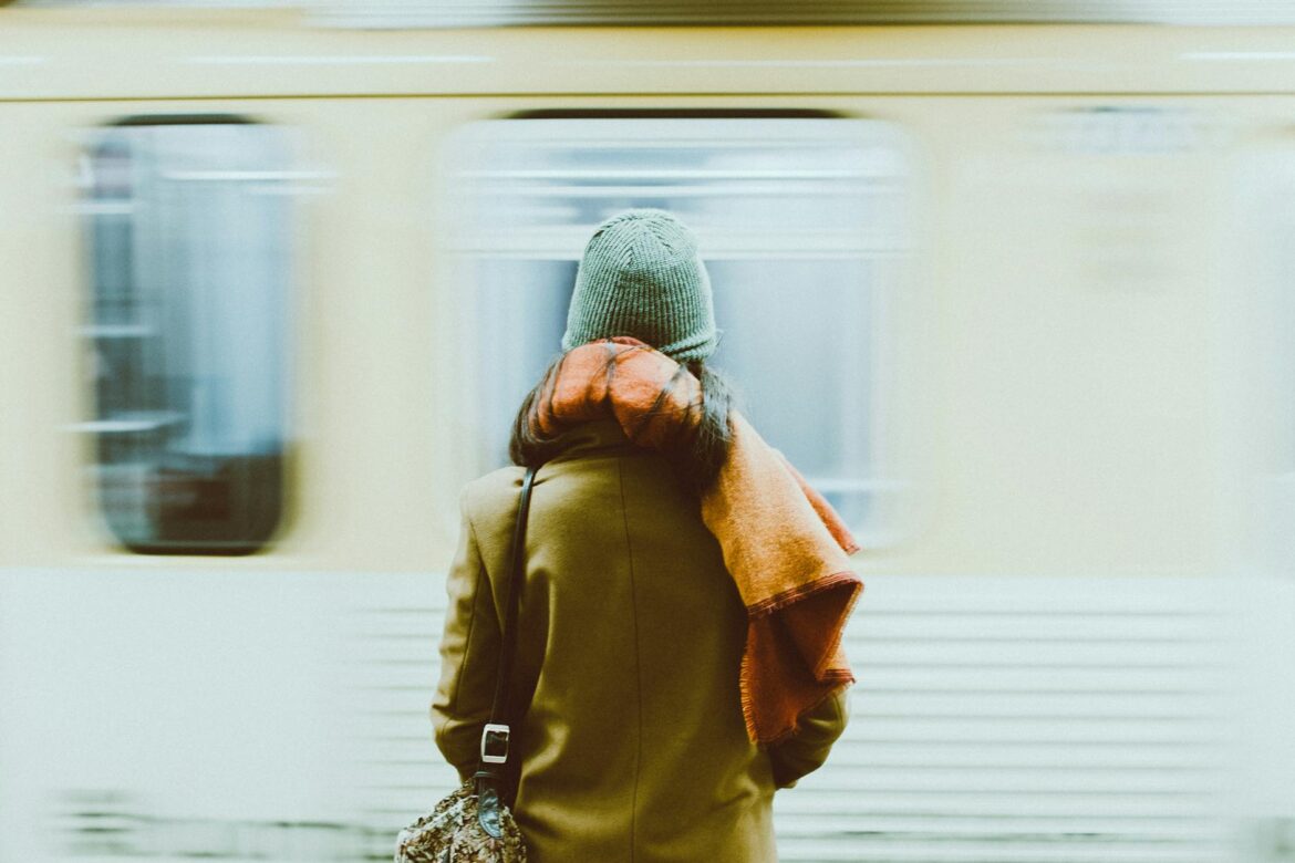 Une personne de dos face à un train qui arrive en gare